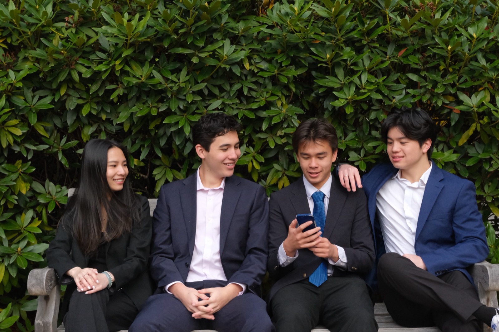 Four members on a bench leaning in over a phone